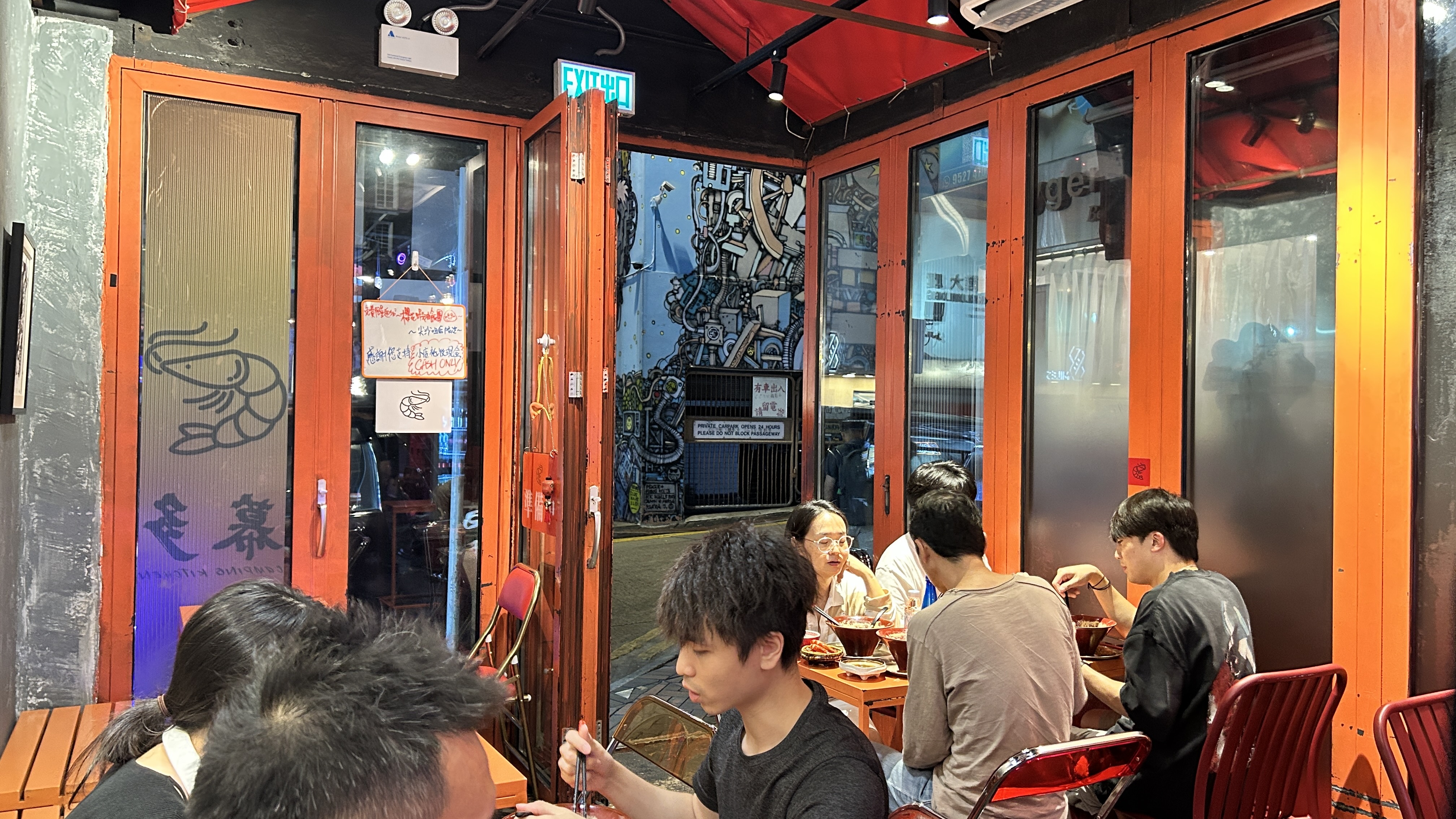 幕多尖沙咀店內：橙色枱、紅色摺椅、窗外窄巷同壁畫，門上現金告示