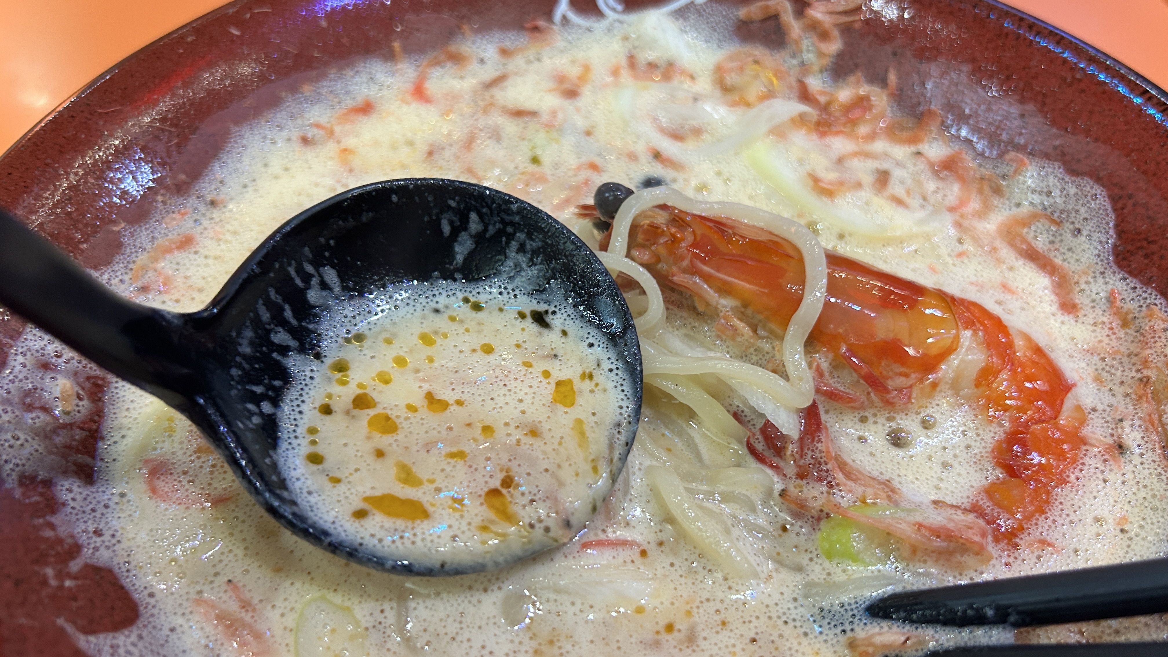 勺子舀起幕多蝦湯，可見泡沫湯面同橙紅蝦油珠